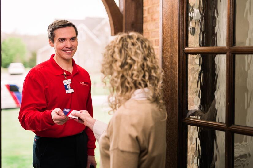 Man wearing a red shirt in doorway handing woman a business card